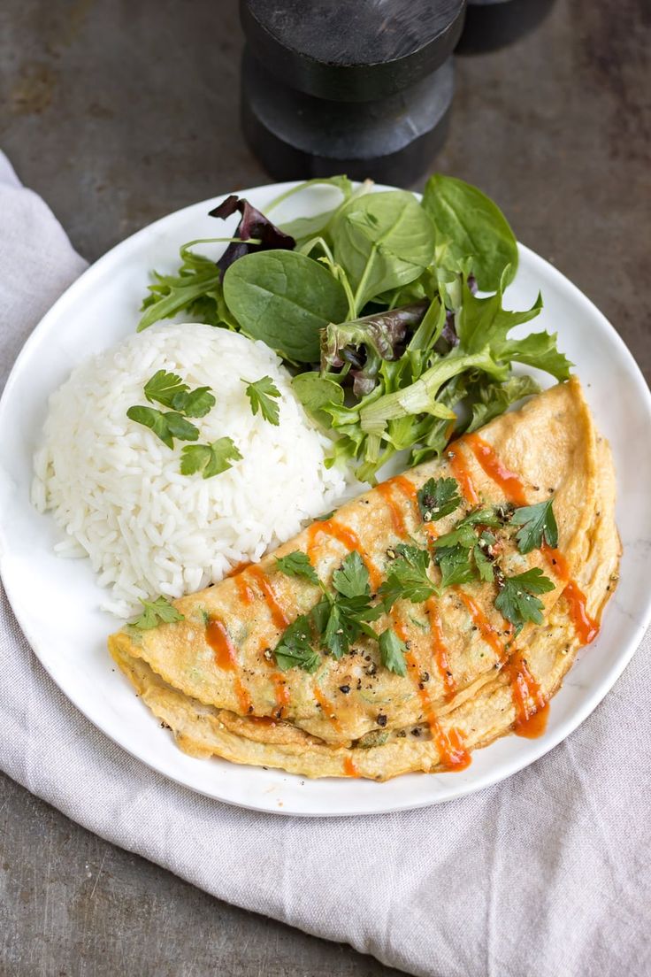 a white plate topped with meat and rice next to a green leafy salad on top of a wooden table