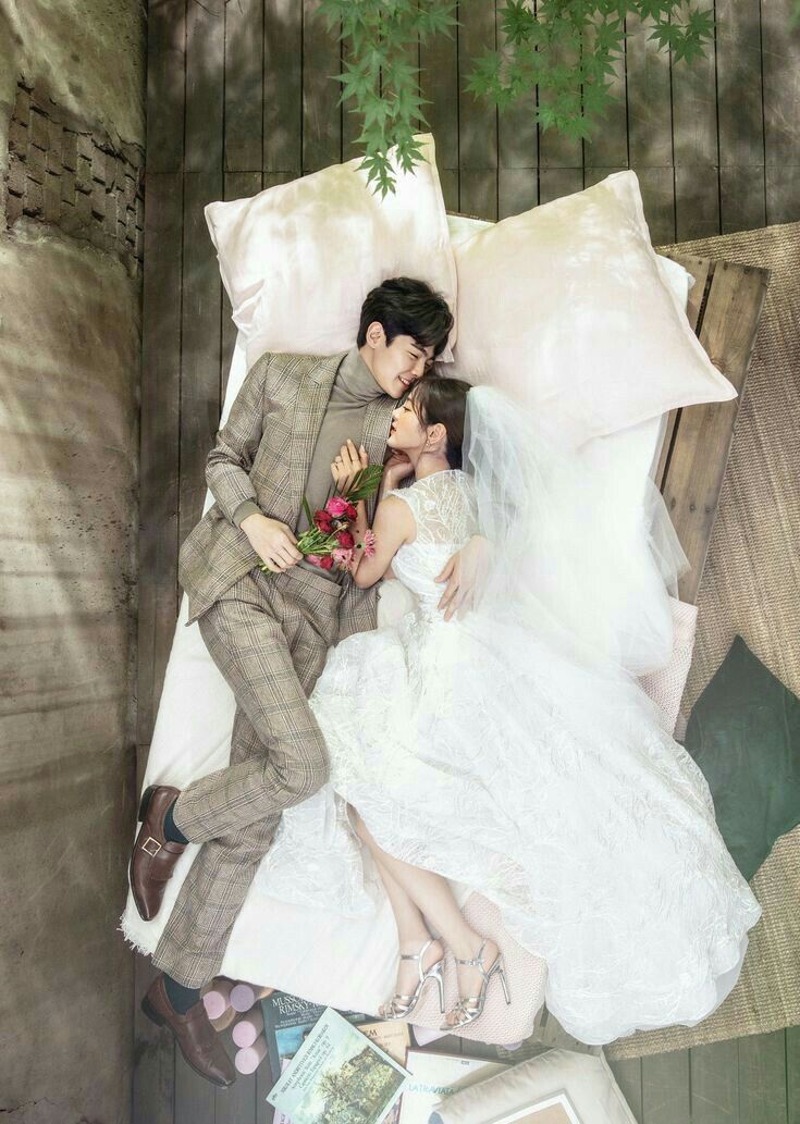 a man and woman laying on top of a bed next to each other under a tree