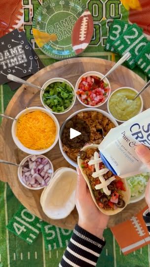 a person holding a bag of food in front of a football field with other foods and condiments