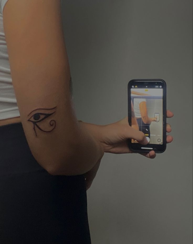 a person holding a cell phone with an eye tattoo on their left side of the arm