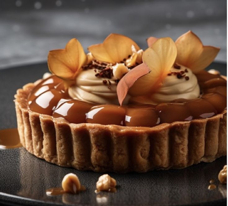 a chocolate tart topped with flowers and nuts on a black plate next to a spoon