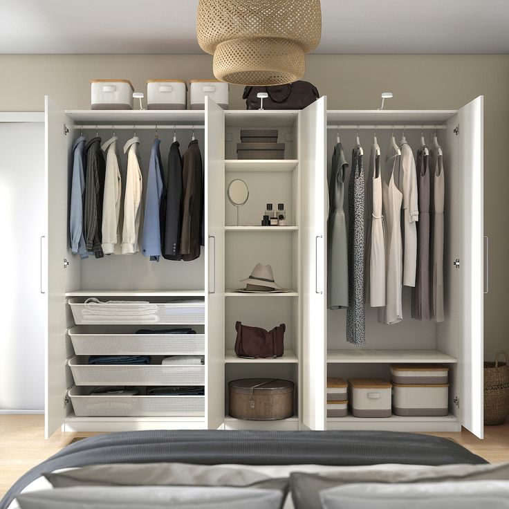 an open closet with clothes, shoes and bags on the shelves next to a bed