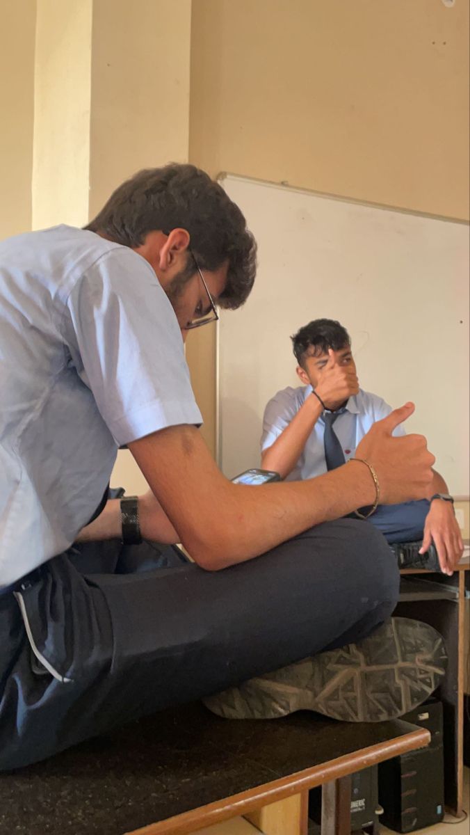 a man sitting on top of a wooden table next to another man in a white shirt and tie