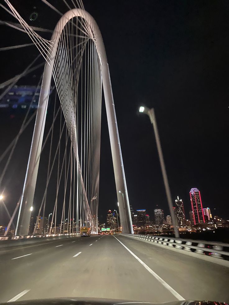 the view from inside a car driving over a bridge at night with city lights in the background