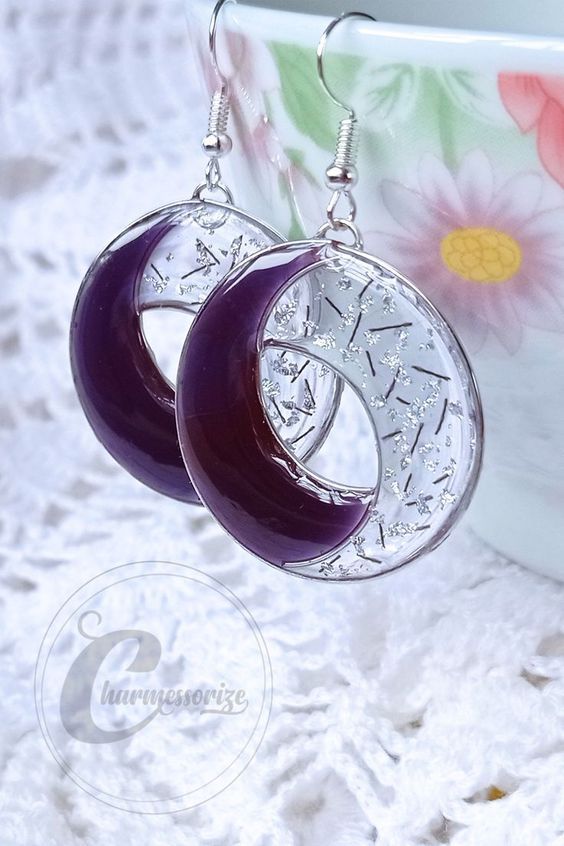 the earrings are made with purple glass and silver plated metal, on top of a white doily