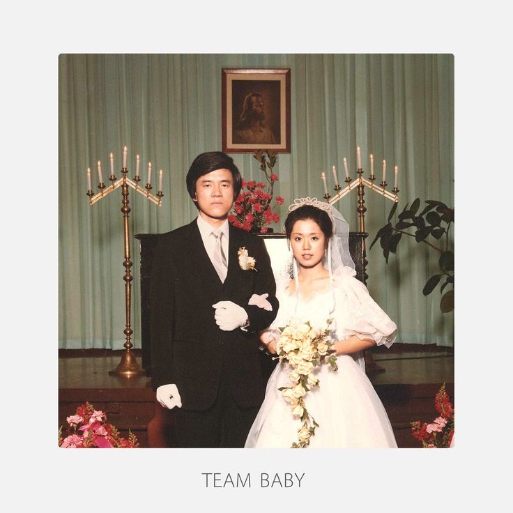 a man and woman in wedding attire standing next to each other with candles on the wall behind them