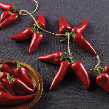 some red peppers are on a table next to a wooden bowl and string with green leaves