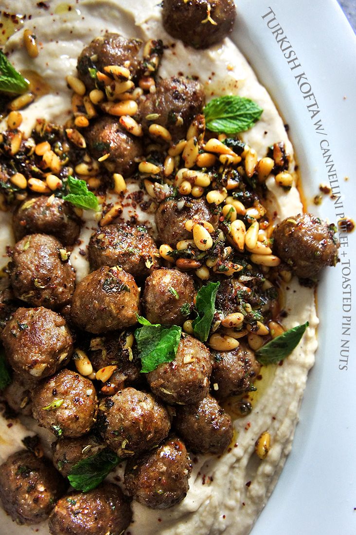 a white plate topped with meatballs covered in sauce and garnished with green leaves