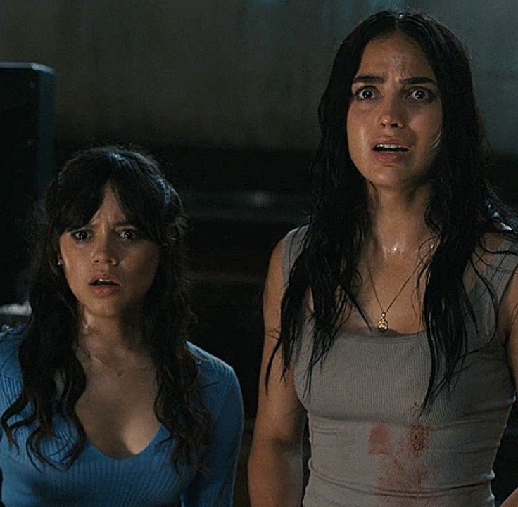 two women standing next to each other in front of a tv screen with blood on it