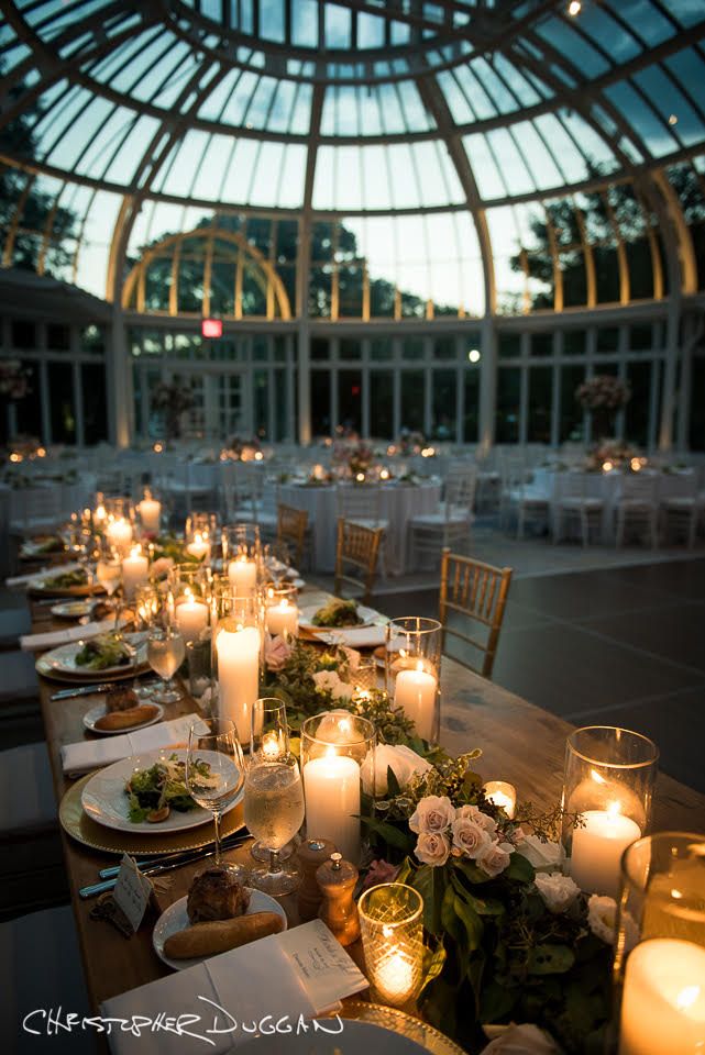 a long table is set with candles and plates for an elegant wedding reception in front of a domed glass building