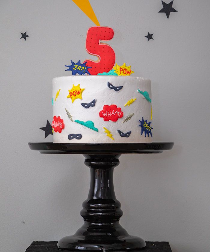 a birthday cake with the number five on it is sitting on a black pedestal in front of a white wall