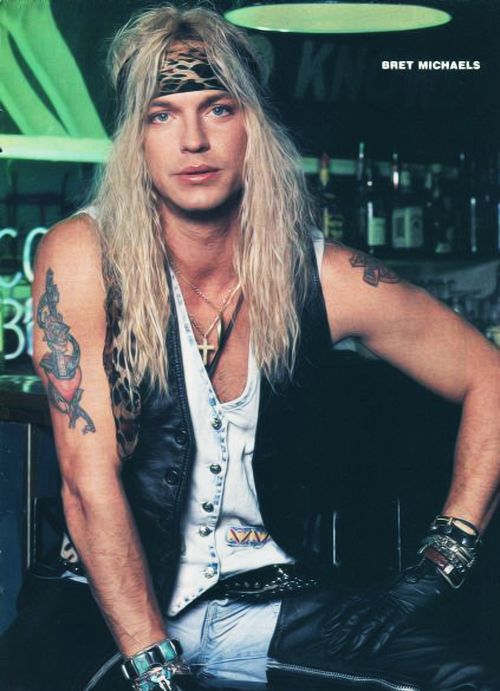 a man with long hair sitting on top of a stool in front of a bar