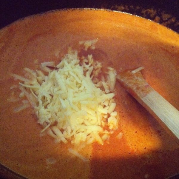 a wooden bowl filled with soup and cheese on top of it's side next to a spatula