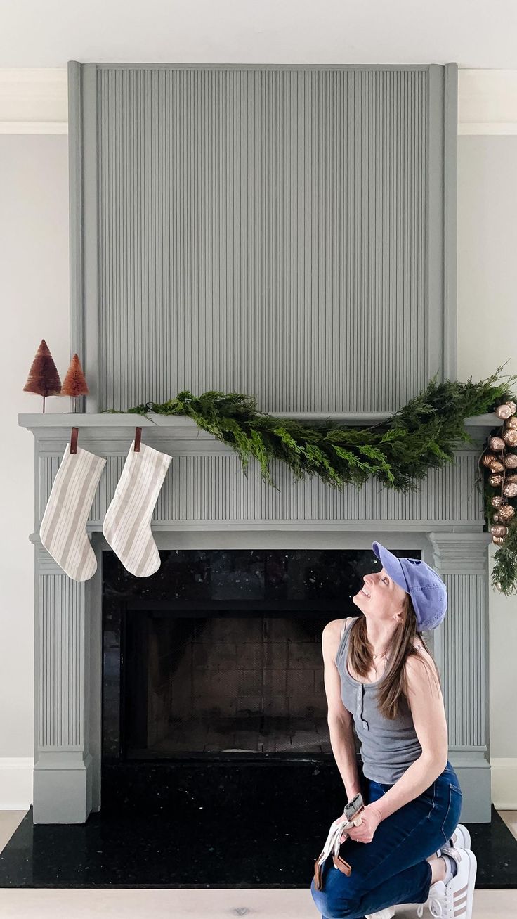 a woman sitting on the floor in front of a fireplace with stockings hanging over it