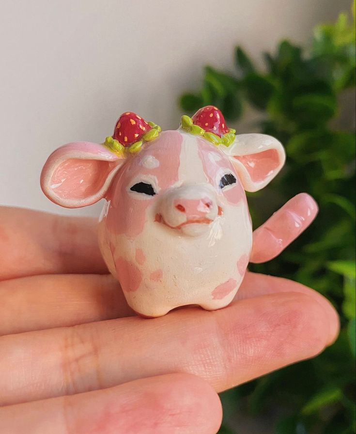 a small pig figurine with two strawberrys on its head sitting in someone's hand