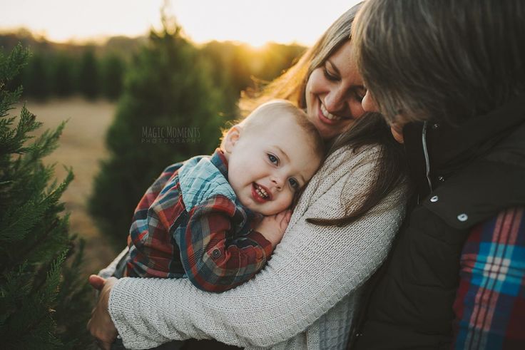 a woman holding a baby in her arms and smiling at the camera while standing next to a christmas tree