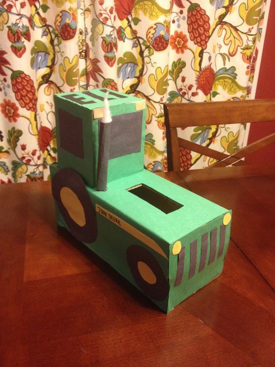 a cardboard box shaped like a tractor sits on a wooden table in front of a curtain