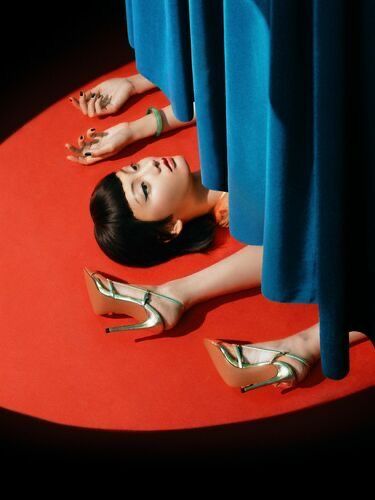 a woman laying on top of a red carpet next to two pairs of high heels