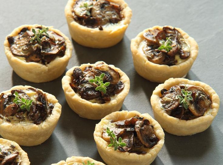 small pastries with mushrooms and parsley in them on a black table top, ready to be eaten