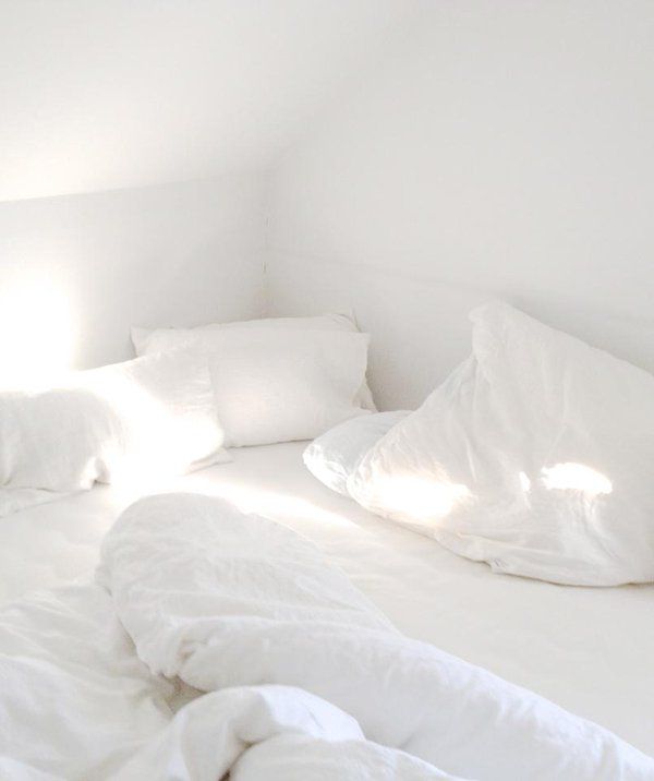 an unmade bed with white sheets and pillows in a room that is mostly white