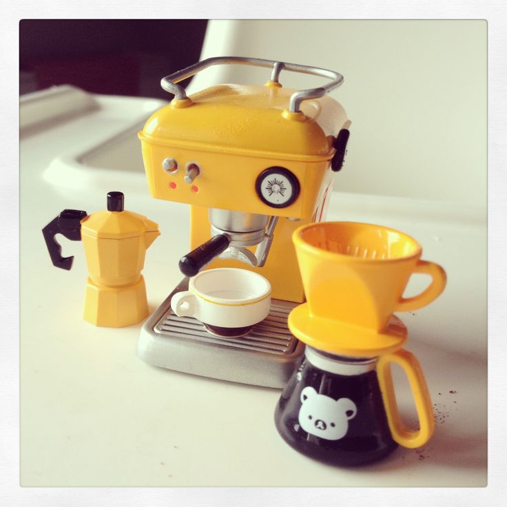 a yellow coffee maker sitting on top of a counter next to cups and saucers