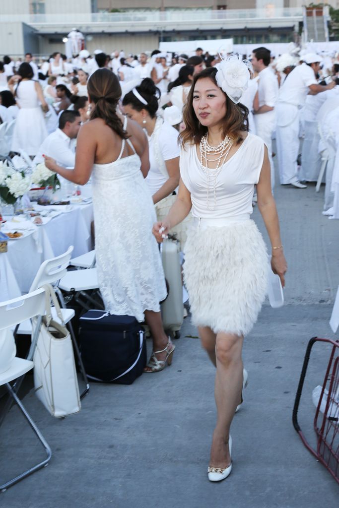 a woman in a white dress walking down a street next to tables with people dressed in white