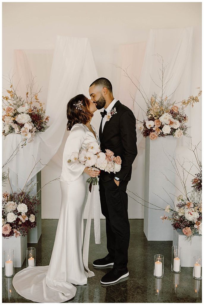 a newly married couple kissing in front of floral arrangements and candles at their wedding ceremony