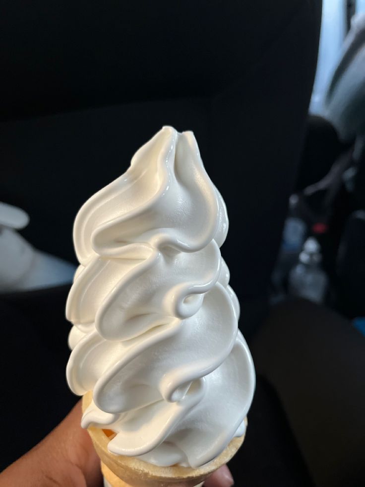 a hand holding an ice cream cone with white frosting on it's top