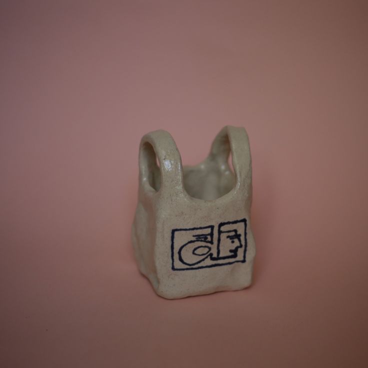 a white ceramic object with a black design on the front and bottom part, sitting on a pink surface