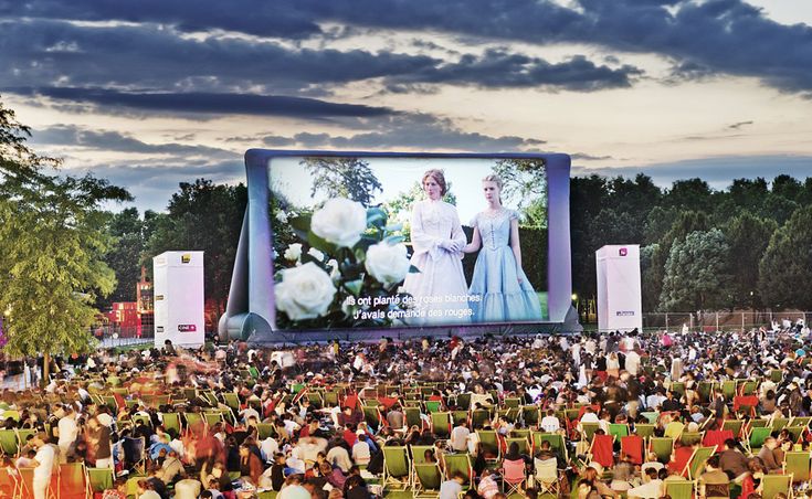 a large group of people sitting in lawn chairs watching a movie on a big screen