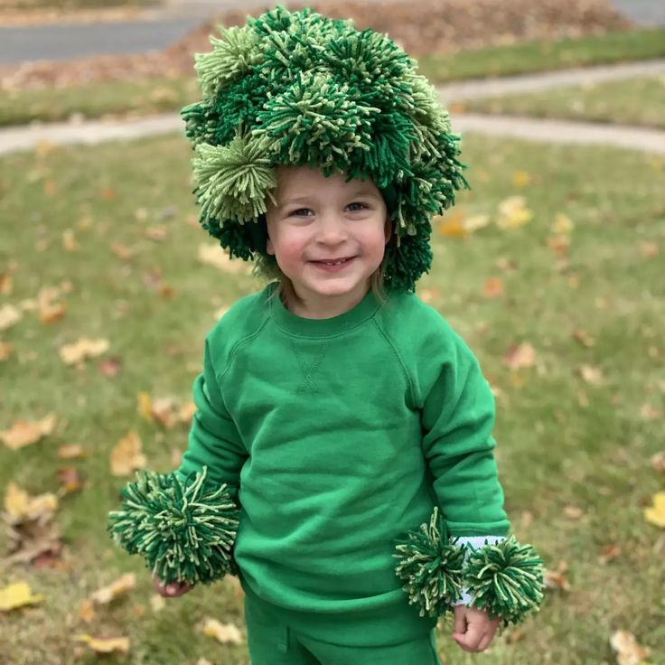 a little boy wearing a green outfit with pom - poms on his head