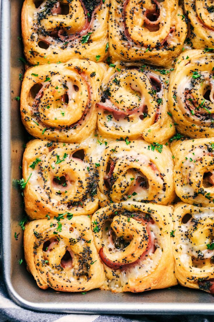 a pan filled with rolls covered in ham and cheese sprinkled on top of each other