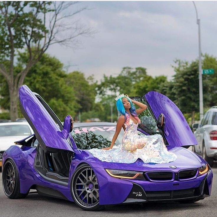 a woman is standing on the hood of a purple sports car with its doors open