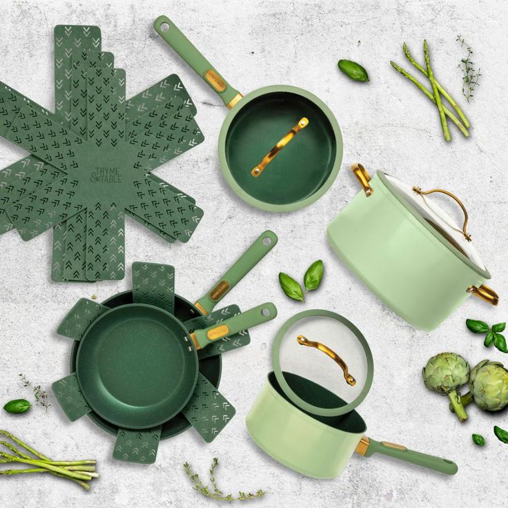 green pots and pans are arranged on a white surface with flowers, leaves and spoons