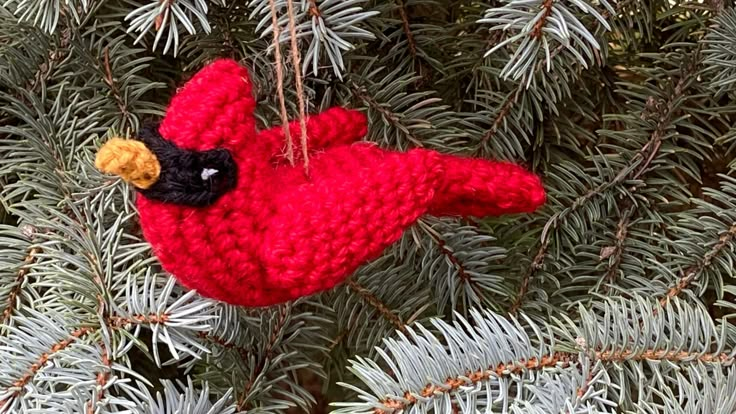 a red bird ornament hanging from a pine tree