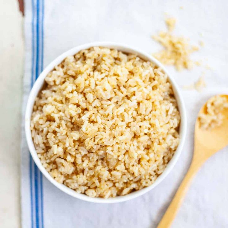 a white bowl filled with brown rice next to a wooden spoon on top of a blue and white towel