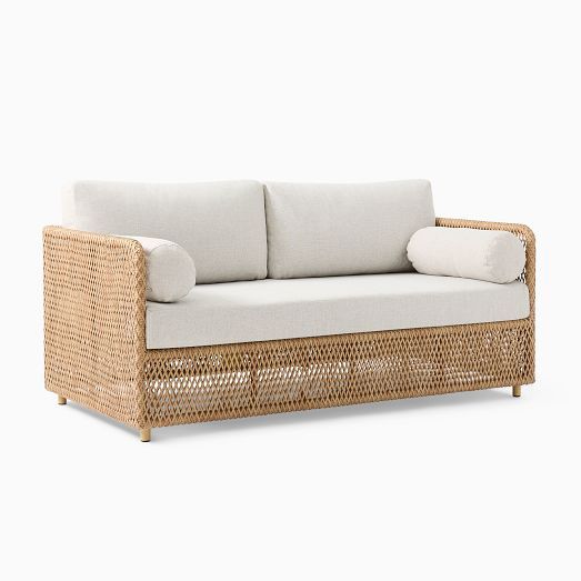 a wicker couch with two pillows on it's back and one arm facing the camera