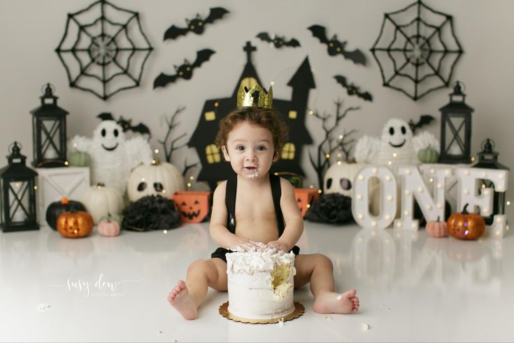 a baby is sitting on the floor with a cake in front of him and halloween decorations behind him