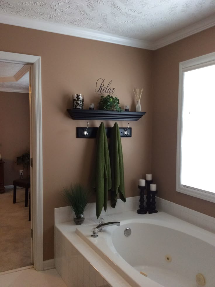 a bath tub sitting under a window next to a wall mounted shelf with towels on it