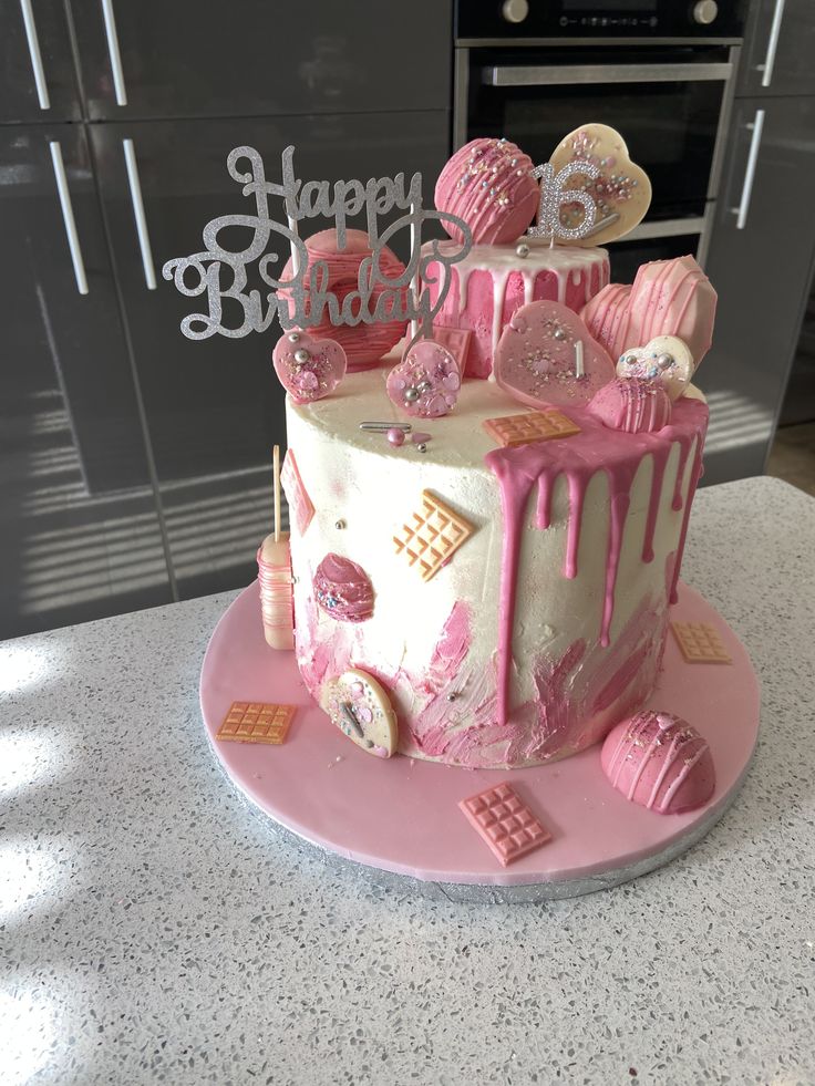 a birthday cake with pink icing and decorations on the top is sitting on a counter