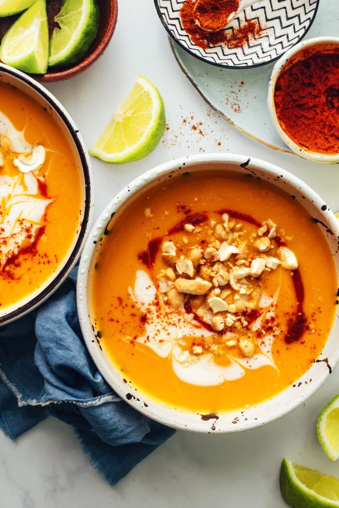 two bowls filled with carrot soup next to limes and other ingredients on a table