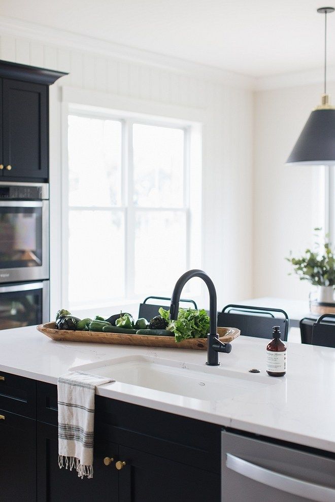 a kitchen with black cabinets and white countertops has an island in front of the sink