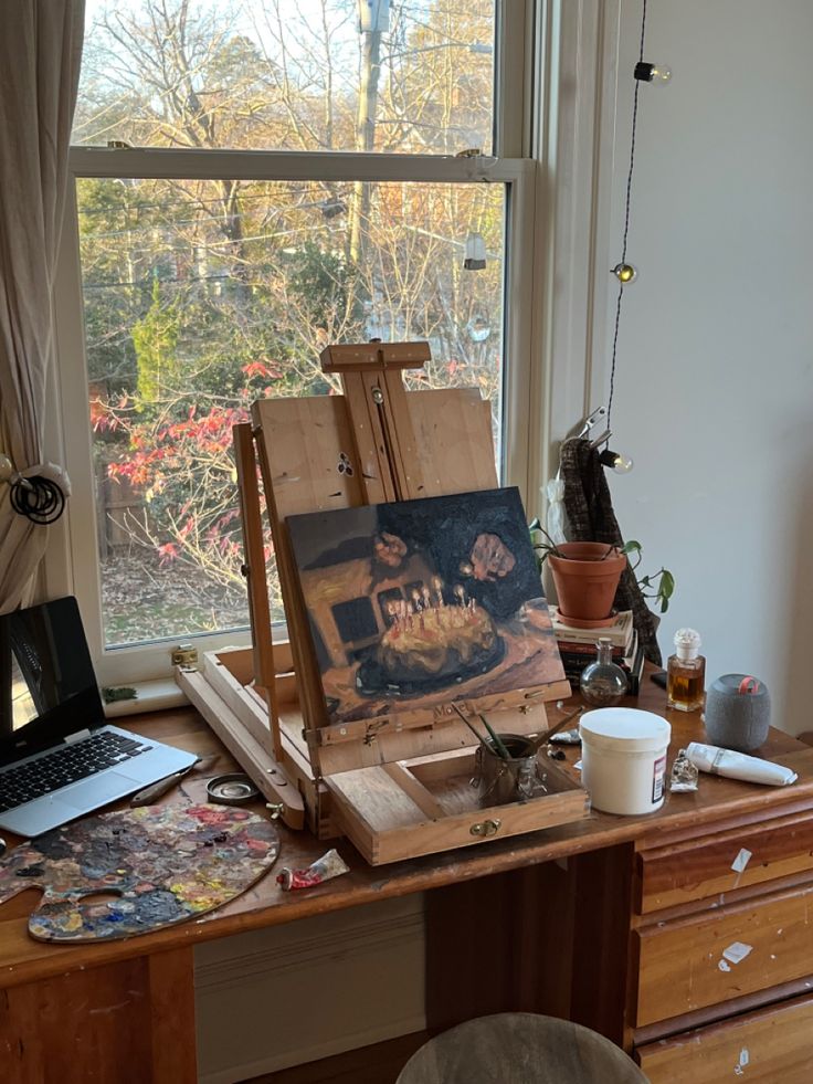 an artist's easel sitting on top of a wooden desk next to a window