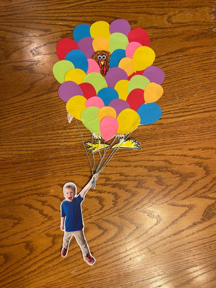 a young boy holding onto a bunch of balloons on a wooden table with a sticker attached to it