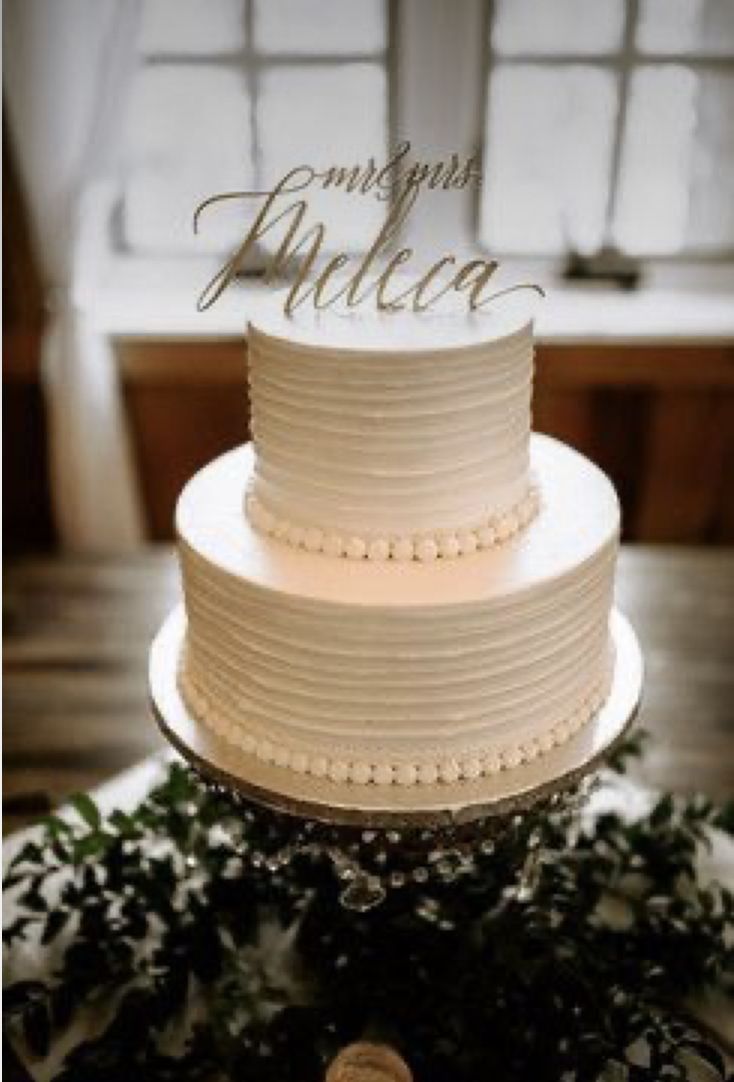 a white wedding cake sitting on top of a table next to a window with greenery