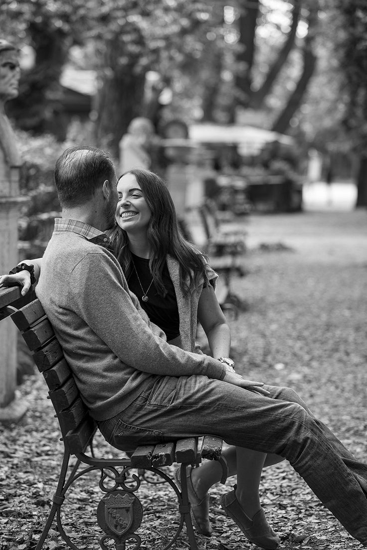 a man and woman are sitting on a bench in the park, looking into each other's eyes