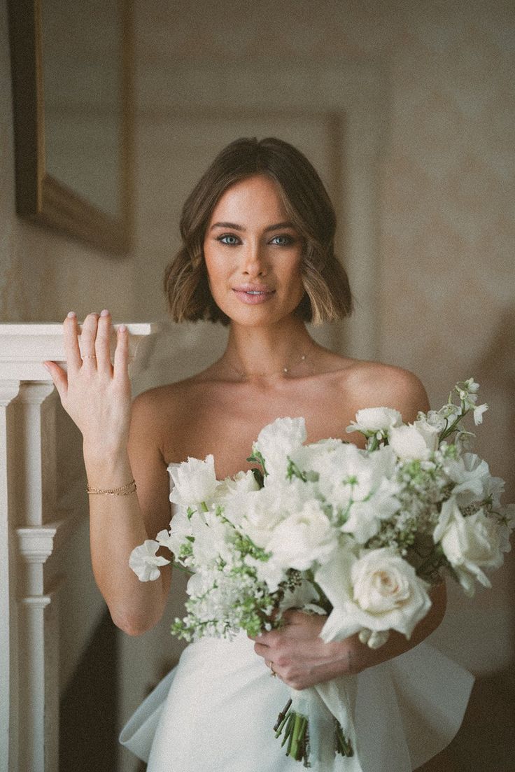 a woman holding a bouquet of flowers in her hand and posing for the camera while wearing a wedding dress