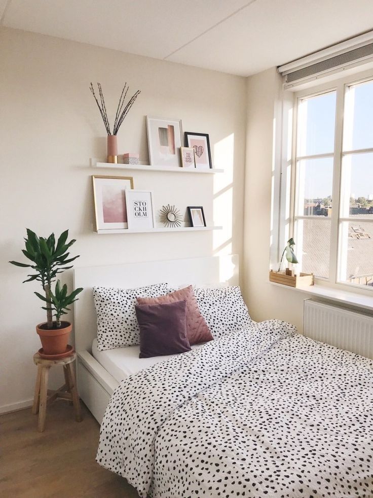 a bed sitting under a window next to a potted plant on top of a wooden floor