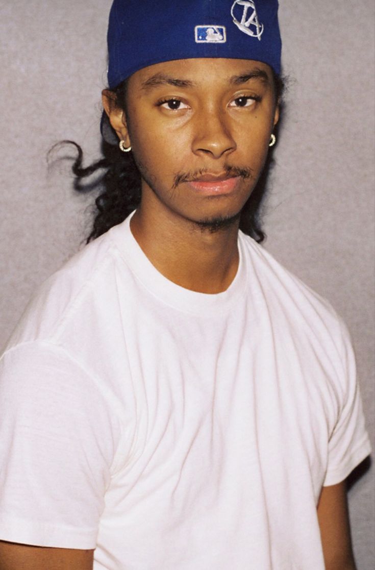 a young man wearing a blue hat and white t - shirt is looking at the camera