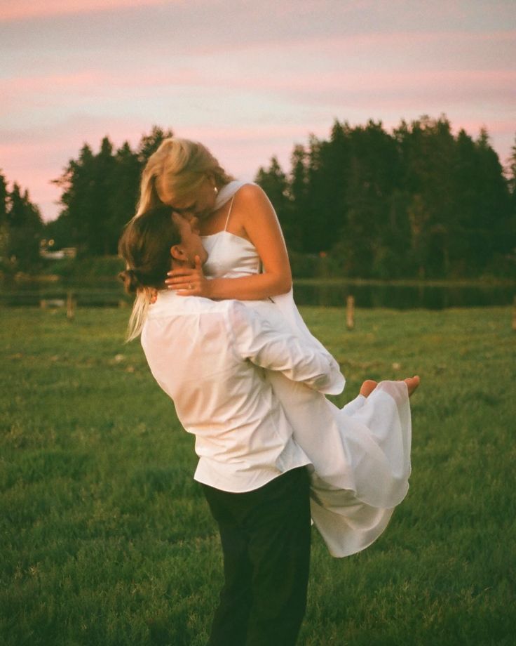 a man is holding a woman in his arms while they are standing in the grass